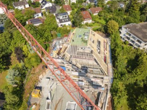 Crane over a construction site with an unfinished roof and surrounding residential buildings,