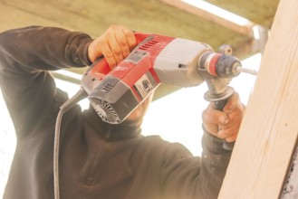 A worker uses a drill on vertical wooden surfaces, carpentry construction site, roof extension,