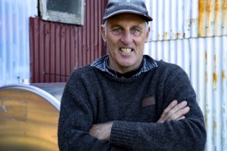 Man wearing cap smiles in front of corroded metal wall in Wilson Bay