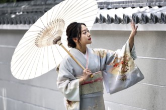 Woman wearing kimono with umbrella gesturing in front of a wall, Kyoto, Higashiyama, Japan