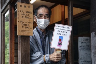 Ticket checker at Kiyomizu Temple in Kyoto wearing a mask and holding an information sign, Kyoto,