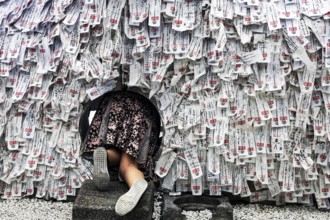 Person crawling through hole in stone with strips of paper in Yasui Konpiragu Temple, Kyoto, Gion,