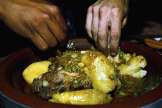 Hands serving a traditional Moroccan dish with lamb and potatoes for dinner, Errachidia, Morocco