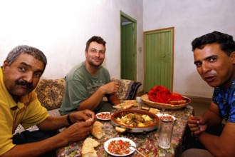 Three men enjoy a Moroccan dinner together with bread and a hearty dish, Errachidia, Morocco