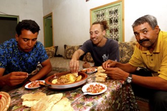 Three men share a traditional Moroccan dinner in a hospitable atmosphere, Errachidia, Morocco