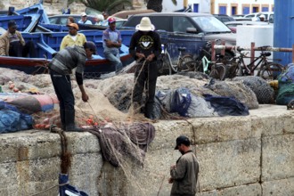 Fishermen unravel nets on a harbor wall in Essaouira, Essaouira, Morocco