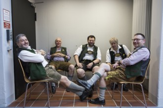 Five people in traditional costumes sit in a corner between two halls at the Green Week on the
