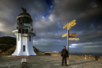Lighthouse and yellow signpost at Cape Reinga under dramatic sky, Cape Reinga, Northland, New
