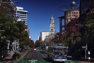 Queen Street with bus traffic, skyscrapers and clock tower under clear sky, Auckland, New Zealand