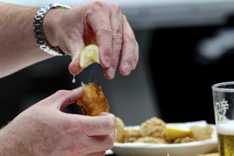 Hands squeeze lemon over fried food at Wynard Quarter Fish Market, Auckland, North Island, New