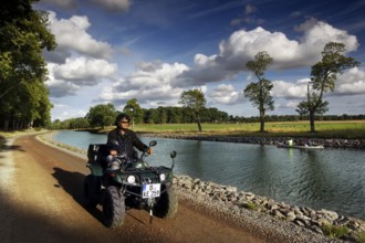 Person on an ATV rides along the Göta Canal in Borensberg under a blue sky, Borensberg, Sweden
