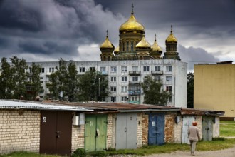 Prefabricated building in front of cathedral with golden domes and garages under dramatic sky,