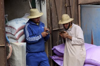 Two men in traditional hats are talking relaxed at a market in Achaouikh, Achaouikh, Morocco