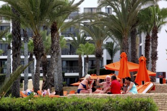 Hotel guests relax on Agadir beach, surrounded by palm trees and umbrellas, Agadir, Morocco