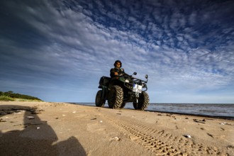 Person riding on ATV along the beach under a cloudy sky, Kolka, Latvia