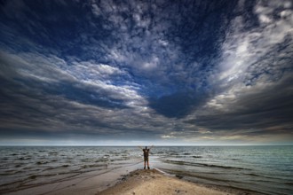Man on sandy beach with dramatic clouds above sea near Cape Kolka, Kolka, Latvia