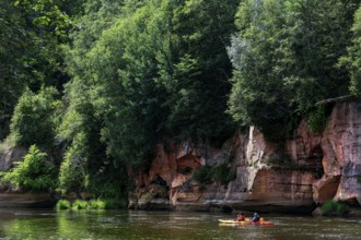 Rocks on Gauja river in national park with dense vegetation and canoes in water, Gauja National