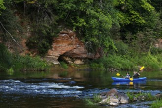 Two people in a canoe paddle through Gauja National Park along the imposing rocks, Gauja National