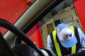 Worker wearing cap and vest bends kindly in front of a car, Kobe, Hyogo, Japan