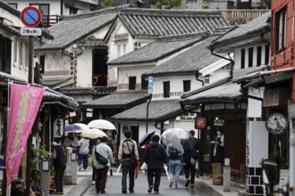 People with umbrellas walk through a historic street with traditional buildings in Kurashiki,