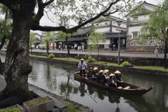 People in a traditional boat on a quiet canal surrounded by historic buildings, Kurashiki, Japan