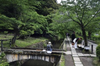 Painter on a Tetsugaku no Michi bridge surrounded by green nature and walkers, Kyoto, Okazaki,