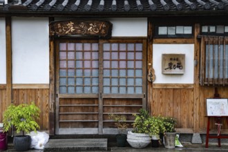 Entrance of a traditional Japanese building with decorated wooden door and potted plants,