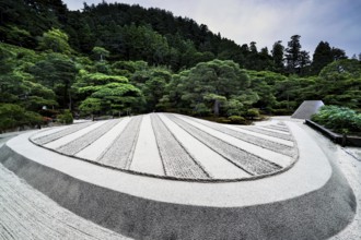 Zen garden of Ginkaku-ji Temple with precise sand patterns and rocks surrounded by green landscape,