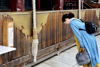 Woman praying in front of a massive wooden shrine at Yasaka-jinja Temple, Kyoto, Higashiyama, Japan
