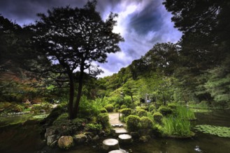 Stepping stones lead through the green garden under a dramatically cloudy sky, Kyoto, Okazaki,