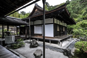 Zen garden with traditional pavilion surrounded by carefully arranged rocks and green vegetation,