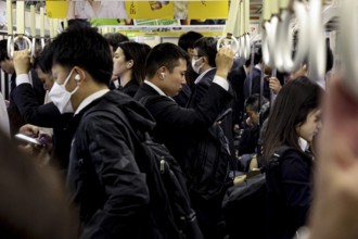 Commuters crowd the Osaka subway, many wearing suits and using smartphones, Osaka, Japan