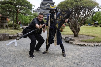 A samurai in traditional costume poses with a visitor in front of Matsumoto Castle, Matsumoto,