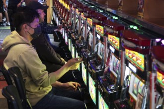 Men playing pachinko on sparkling machines, intense game atmosphere, Osaka, Japan