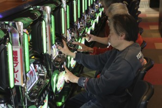 Men play pachinko on bright machines in a lively setting, Osaka, Japan
