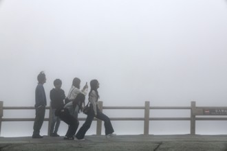 Tourists pose in front of fog-covered crater in Aso, Aso, Japan