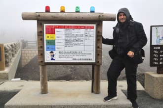 Person standing next to a warning sign in the fog of Nakadake Crater, Aso, Kumamoto, Japan