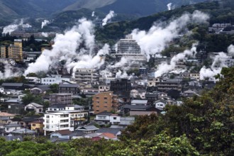 Urban landscape crossed by columns of steam, mountains in the background, Beppu, Oita, Japan