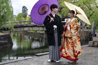A traditionally dressed couple poses with umbrellas at a picturesque bridge, Himeji, Hyogo, Japan