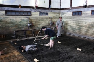 A sand bath at Takegawara Onsen Beppu, one person being cared for by another, Beppu, Oita, Japan