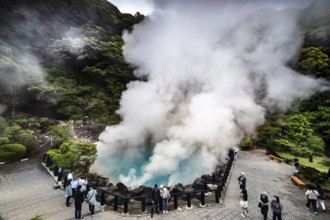 Group of visitors watching steaming blue lake surrounded by rocks and green foliage, Beppu, Oita,