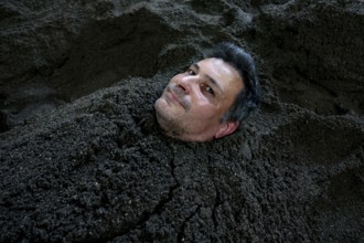 Man buried in sand bath with only his head sticking out, relaxed expression, Beppu, Takegawara