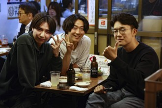 Three friends smile in the cozy atmosphere of a restaurant in the Hoppy-dori, Tokyo, Tokyo, Japan