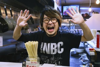 Man at ramen restaurant in Osaka greets with a smile and outstretched hands, Osaka, Japan