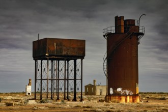 Rusty water towers and orphaned buildings under cloudy outback sky, Oodnadatta Track, null,