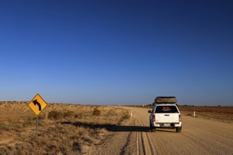 White car on a dusty road with curve sign in the vast outback, Oodnadatta, null, Australia