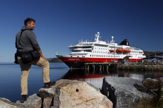 Man on rocks looking at a Hurtigruten ship in Kirkenes harbour, Kirkenes, Finnmark, Norway
