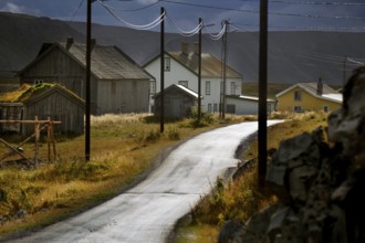 Winding village street with old houses and power lines in cloudy weather, N Hamningberg, null