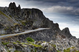 Coastal road nestles against rugged rocks under cloudy skies, N Hamningberg, zero