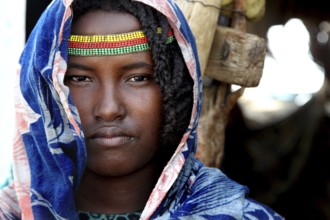 Aishe poses in traditional clothes and colorful accessories in front of Muhammad's hut in Ahmedela,